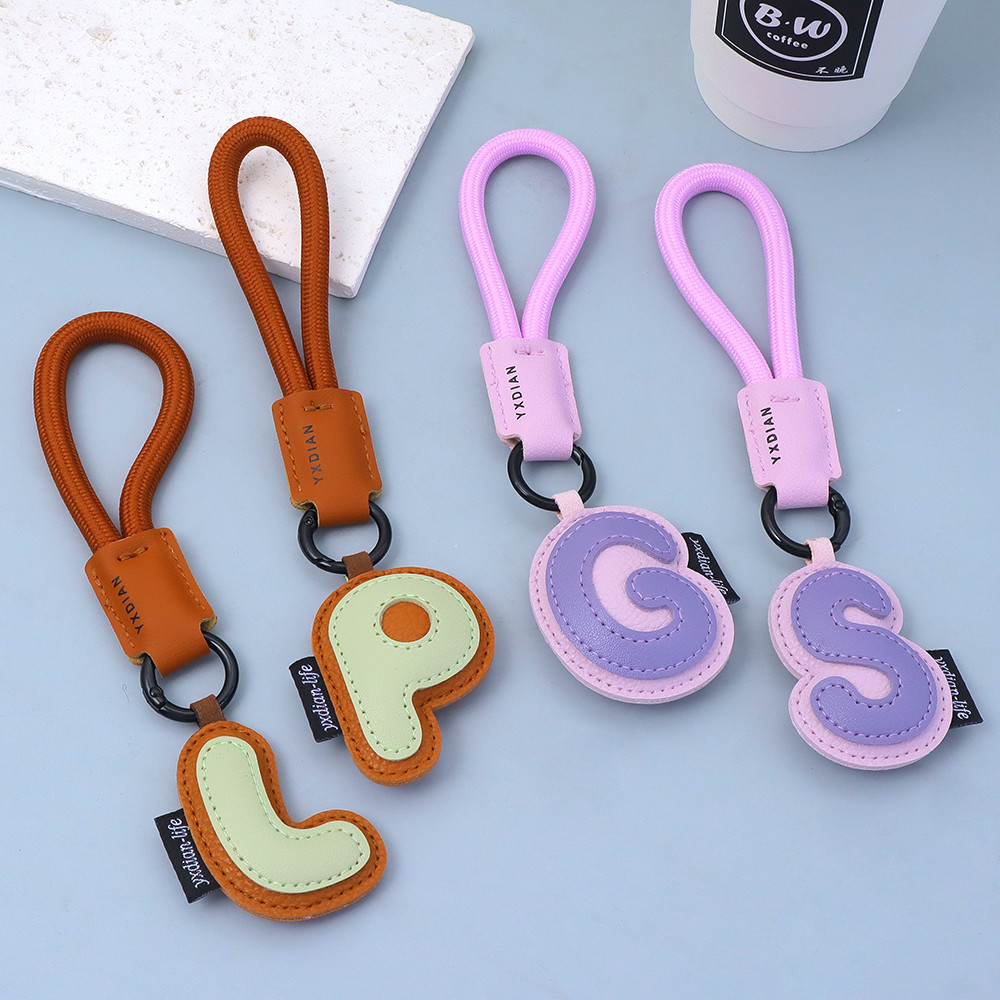 หนังประณีต 26 ตัวอักษรพวงกุญแจแหวนที่มีสีสันป้องกันการสูญหายเชือกถักพวงกุญแจกระเป๋าสาว ทําเอง ออร์นามสกุล อุปกรณ์กุญแจรถ