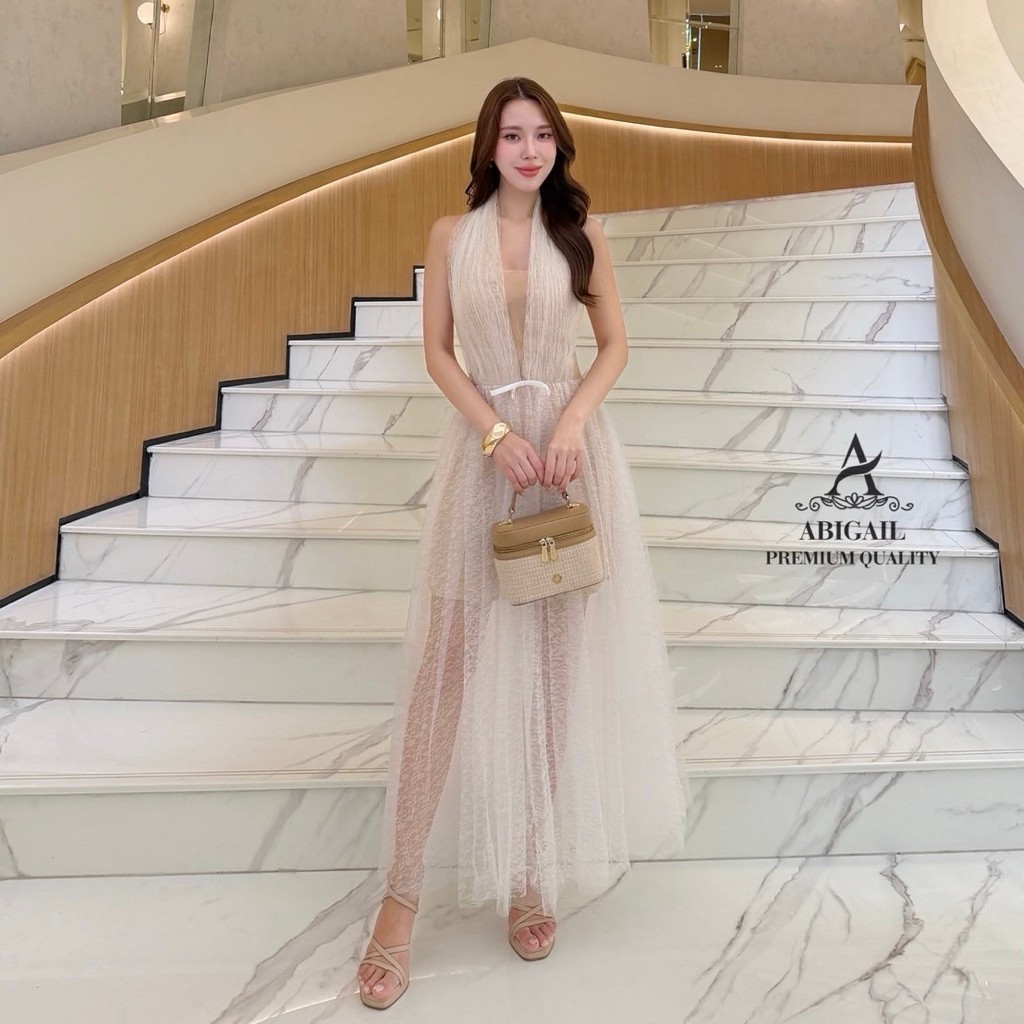 เดรสยาว ดีไซน์คอไขว้คล้องคอ โชว์ช่วงไหล่ โทนสีเบจ-ครีม กระโปรงซ้อนผ้าตาข่ายมุ้ง ซับในสั้น แต่งริบบิ้