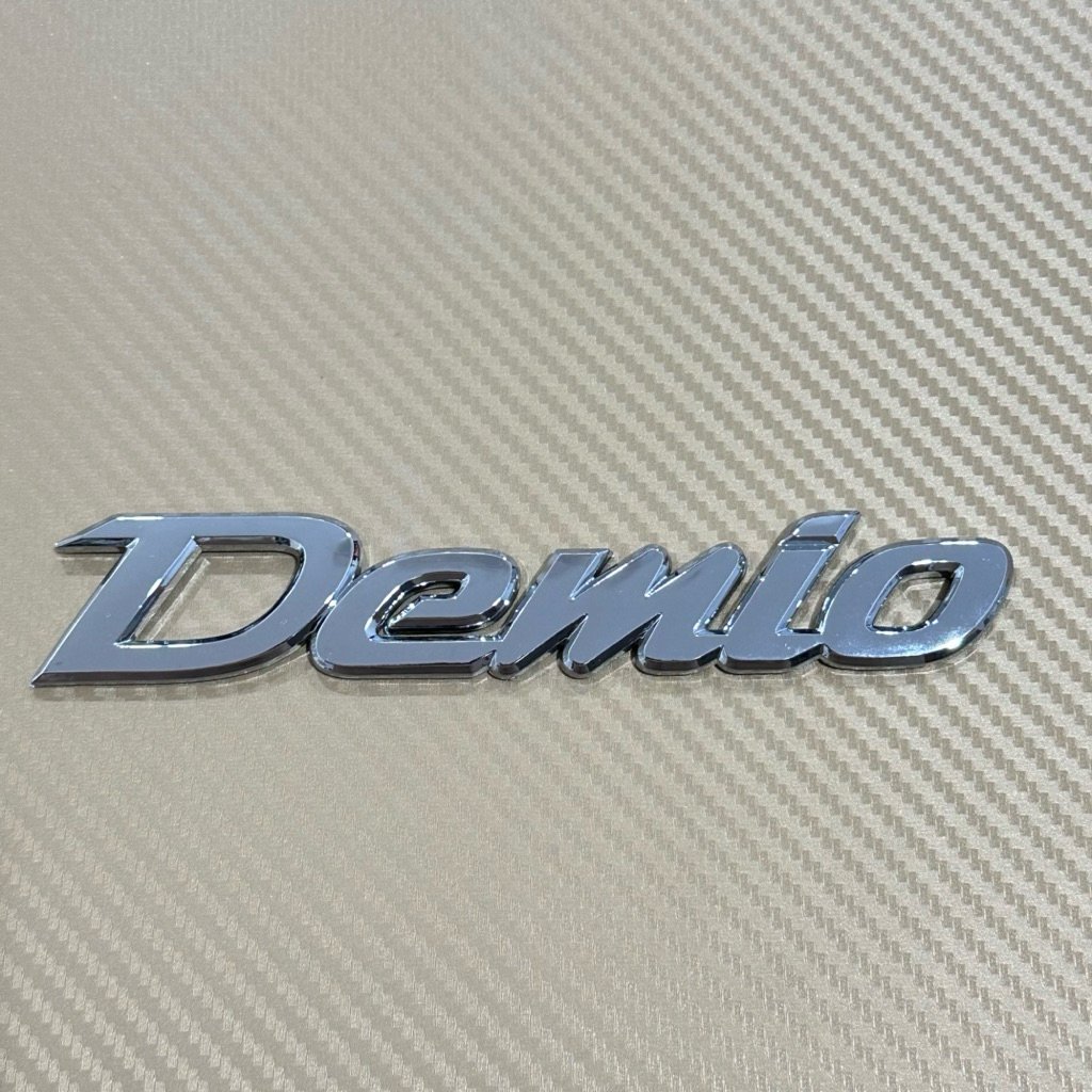 โลโก้ Demio ติดรถ Mazda  ขนาด 2.8 x 15.5 cm ราคาต่อชิ้น