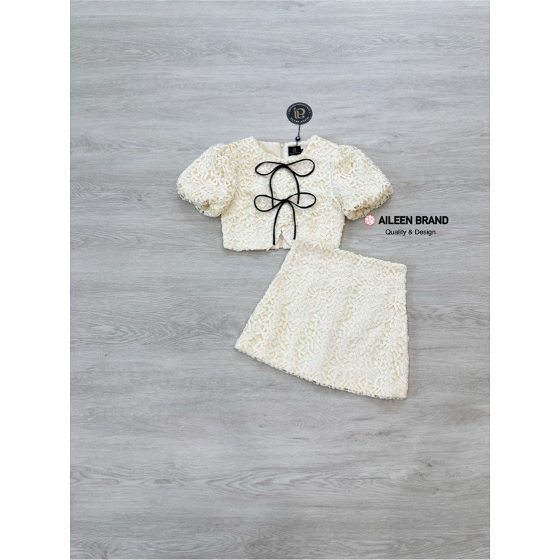 Aileen เสื้อคอป ลูกไม้สีครีม แขนสั้น แต่งจั้มสม๊อคแขน ดีเทลแต่งสายผู้โบว์หน้า มีซิปหลัง แมทซ์กับกระโปรงสั้นลูกไม้
