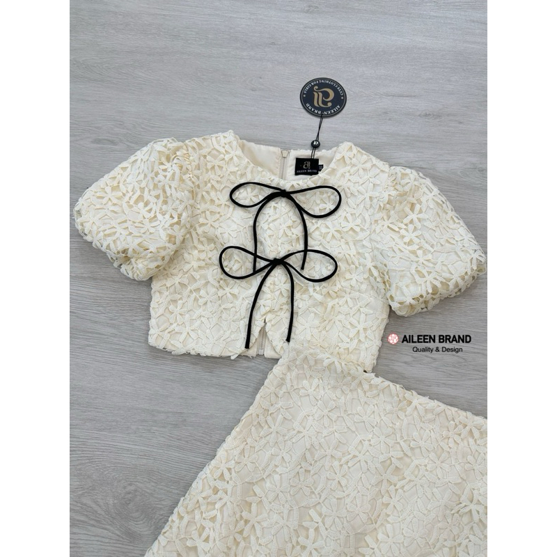 Aileen เสื้อคอป ลูกไม้สีครีม แขนสั้น แต่งจั้มสม๊อคแขน ดีเทลแต่งสายผู้โบว์หน้า มีซิปหลัง แมทซ์กับกระโปรงสั้นลูกไม้