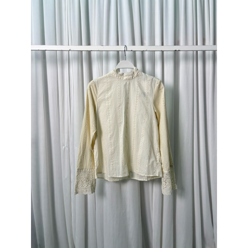 เสื้อเชิ๊ตแขนยาวทรงคอปิดสีเบจผ้าคอนตอน ดีเทลช่วงคอเสื้อกับปลายแขนตัดด้วยผ้าถักโคเชต์ มีกระดุมคอด้านหลัง ปลายแขนมีกระดุม
