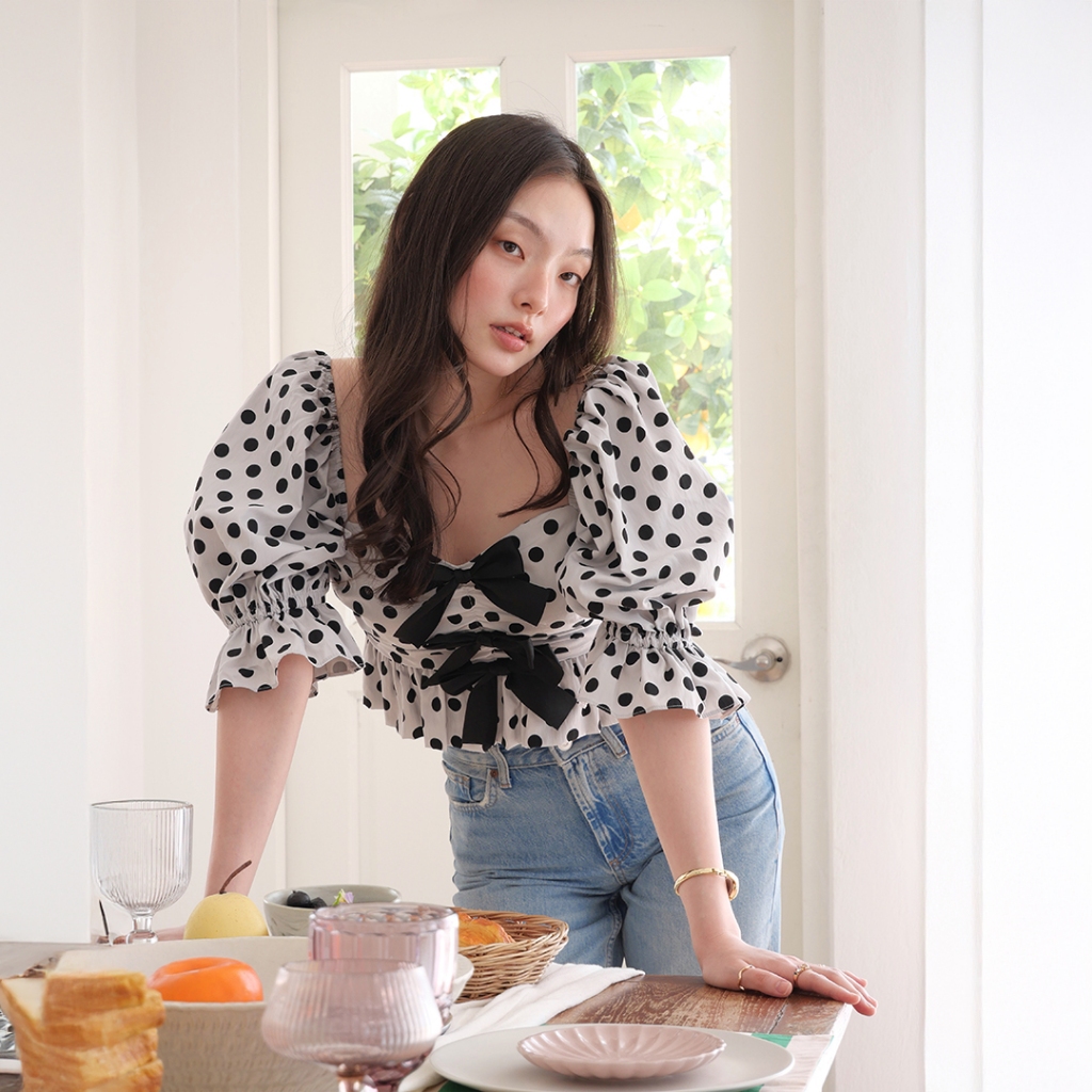 LUCA STUDIO_Willow crop top - เสื้อครอปผ้าโพลีเอสเตอร์ พิมพ์ลายจุด (Polka dot) สีดำบนพื้นสีขาว ตกแต่งโบว์ช่วงอก